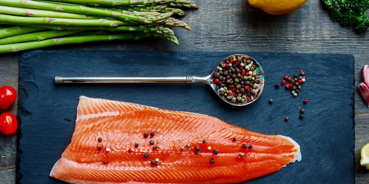 Wild Salmon Filet on cutting board with whole peppercorns and asparagus.