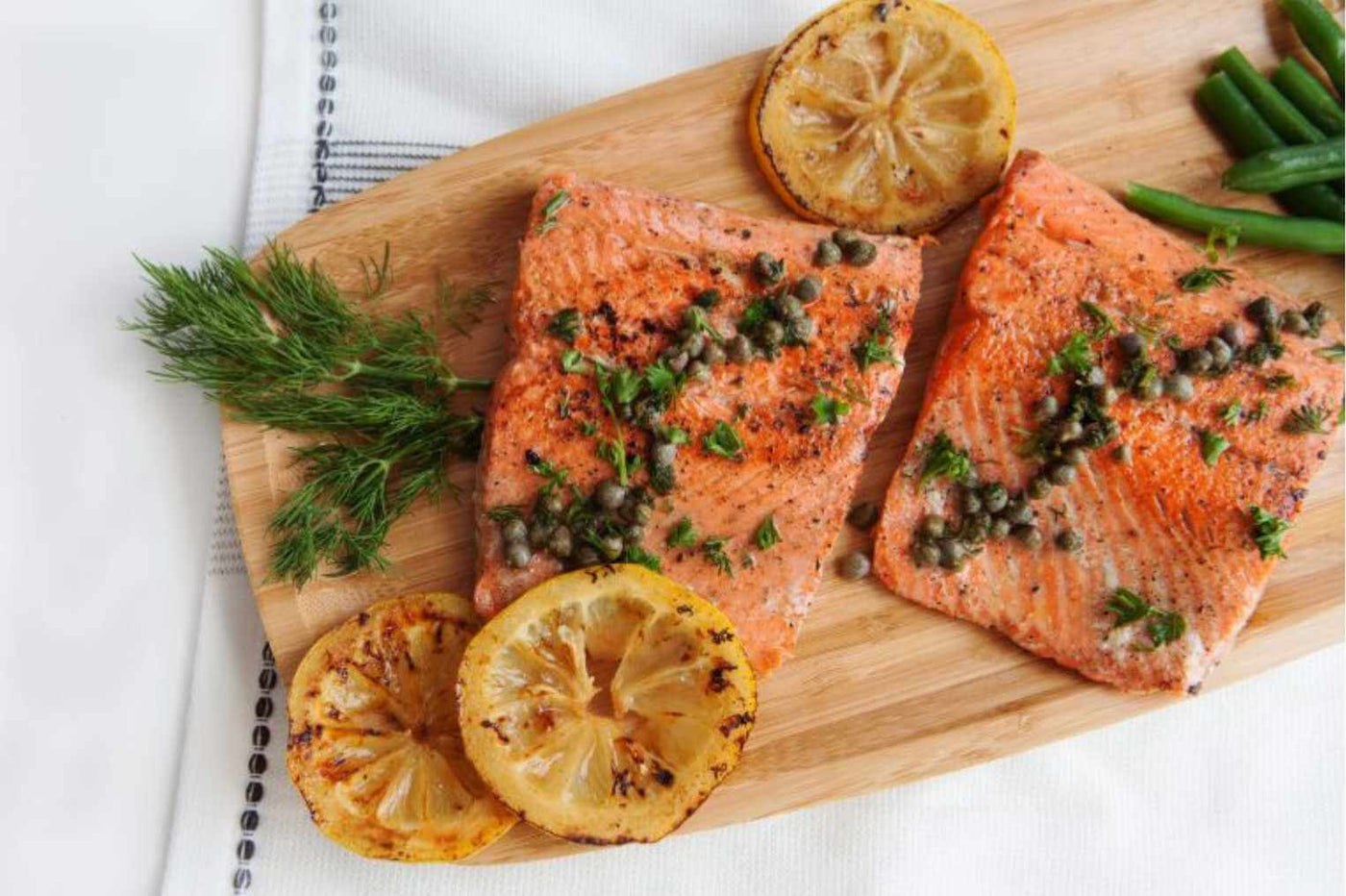 Two cooked wild caught salmon portions on a cutting board with lemon and garnishes.