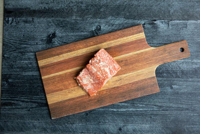 TRADITIONAL WILD CAUGHT SMOKED SALMON ON WOODEN CUTTING SERVING BOARD.