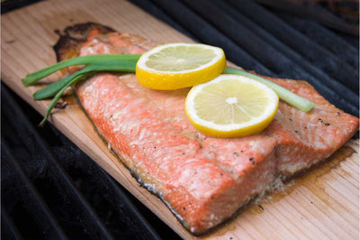 Cooked wild caught salmon filet on a cedar plank with sliced lemon and green onion.