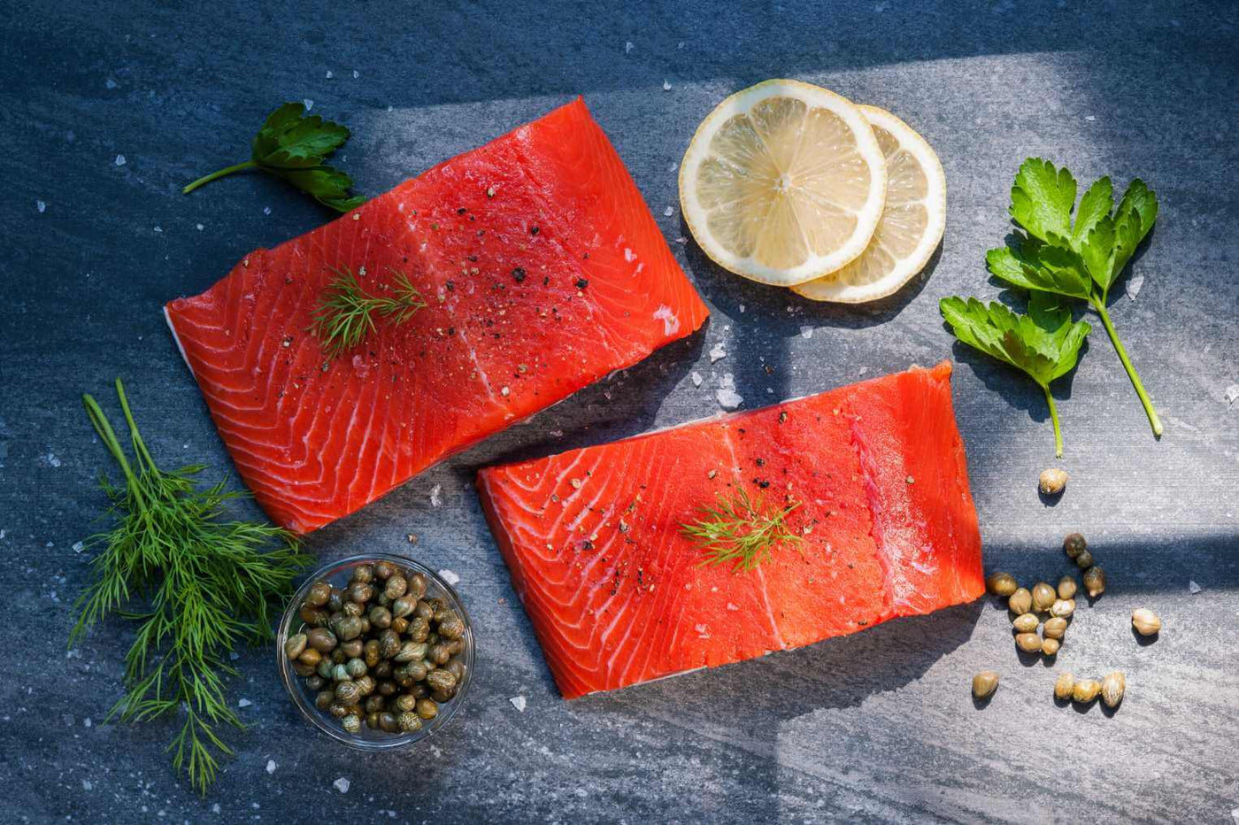 Two Wild Caught Alaskan Sockeye Salmon portions with lemon and seasoning.  Raw, not cooked.