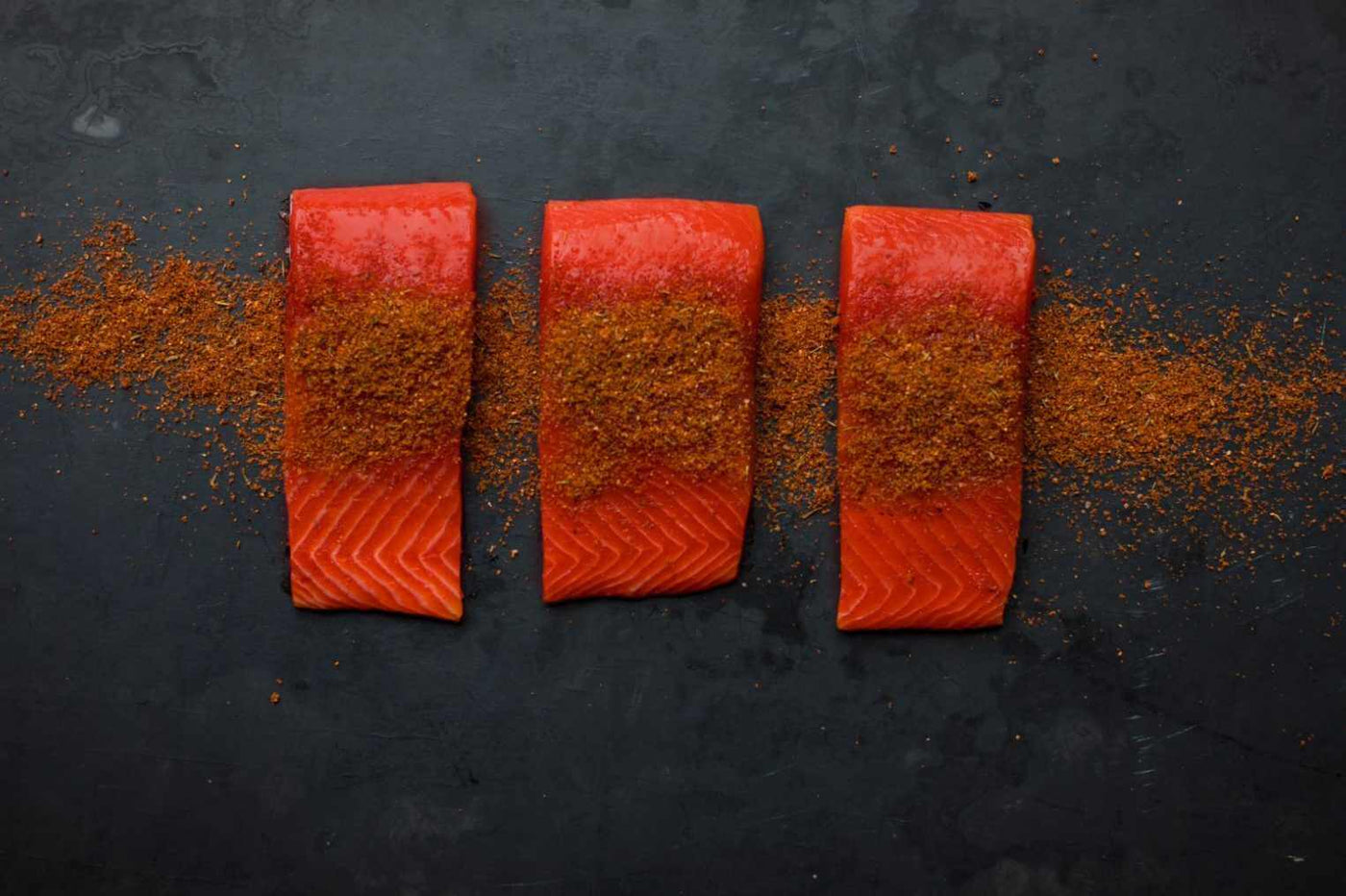 Three wild alaskan salmon portions with seasoning.  Raw not cooked.